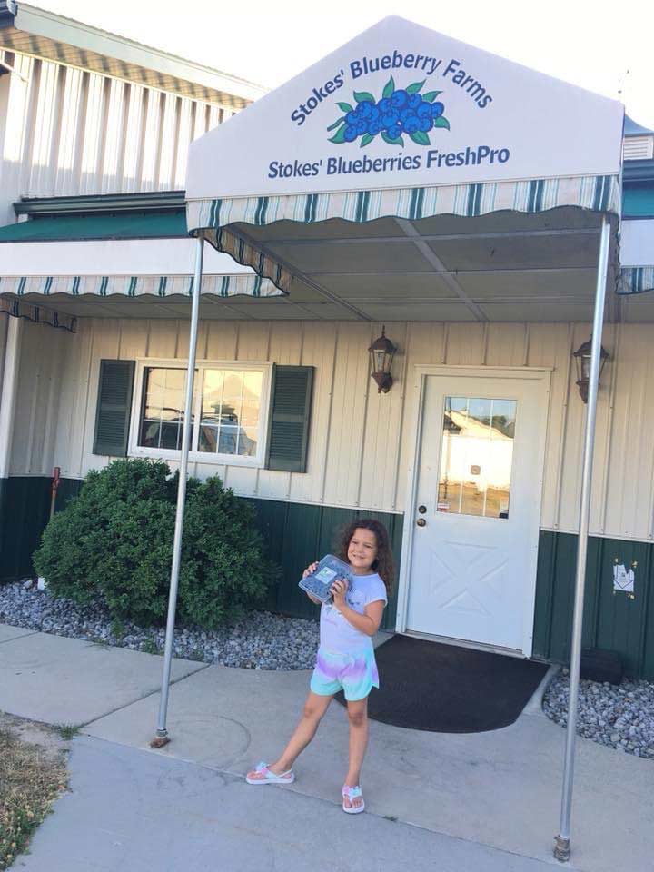 child holding blueberry box in front of entrance